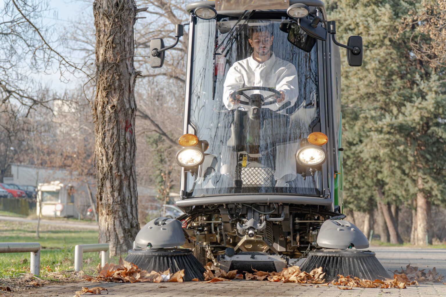 Operator în cabina Green Machines 636, cu periile frontale pe o alee cu frunze