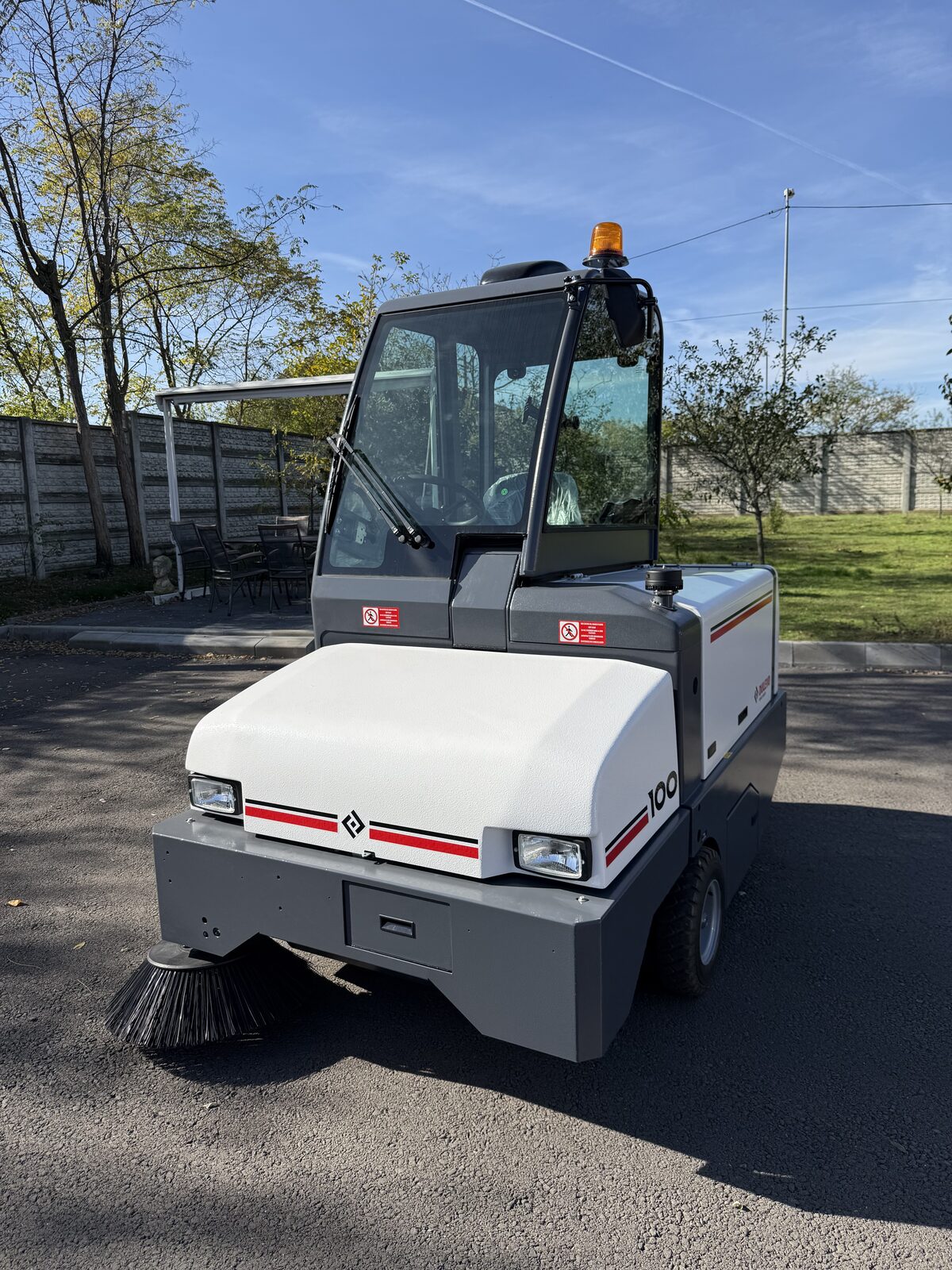 Dulevo 100 văzut din față și din lateral, cu peria coborâtă, pe o platformă asfaltată