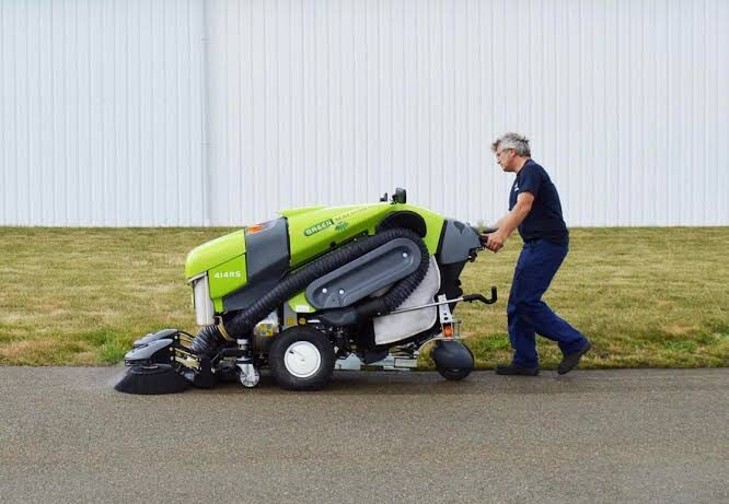 Operator care conduce automăturătoarea Green Machines pe o alee de lângă o clădire